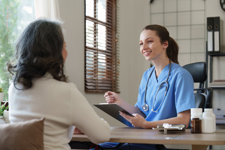 Das Bild zeigt eine Person mit Gesundheitsberuf, die gerade mit einer Patientin im Gespräch ist.
