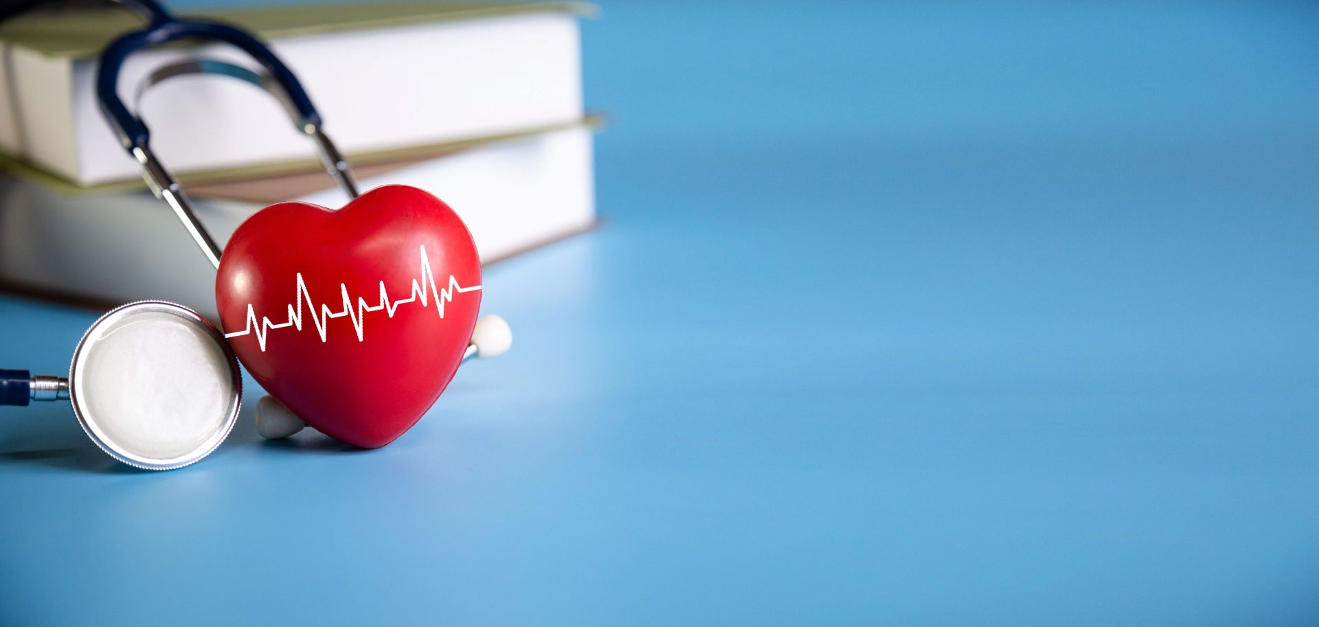 Foto mit einem roten Herz und Herzschlag, daneben ein Stethoskop und Bücher